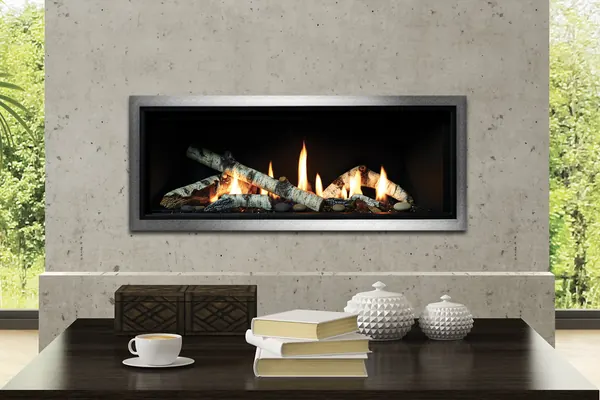 Linear gas fireplace with birch-style logs centered in a concrete wall between garden windows.